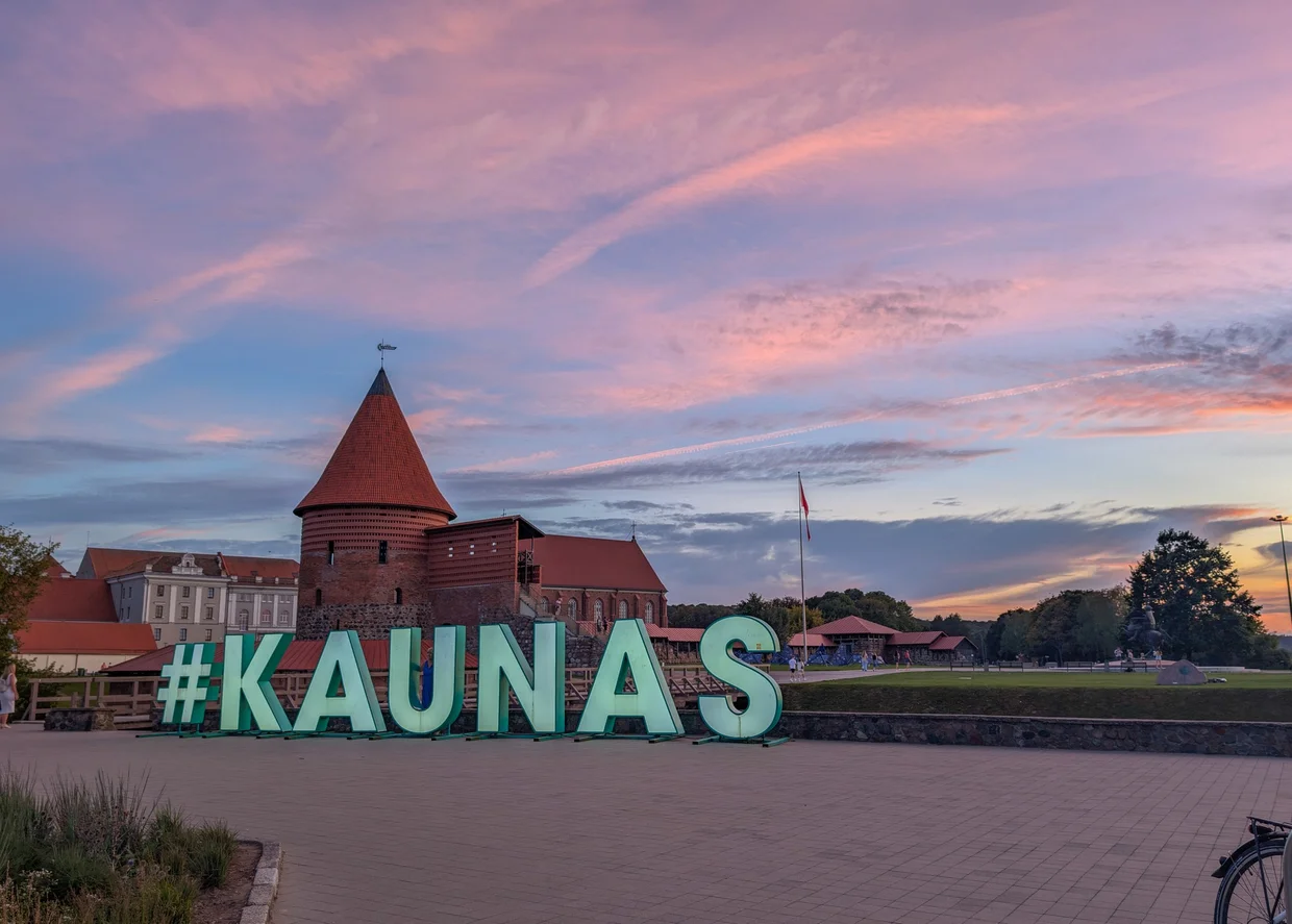 The giant #KAUNAS sign in front of the castle at sunset