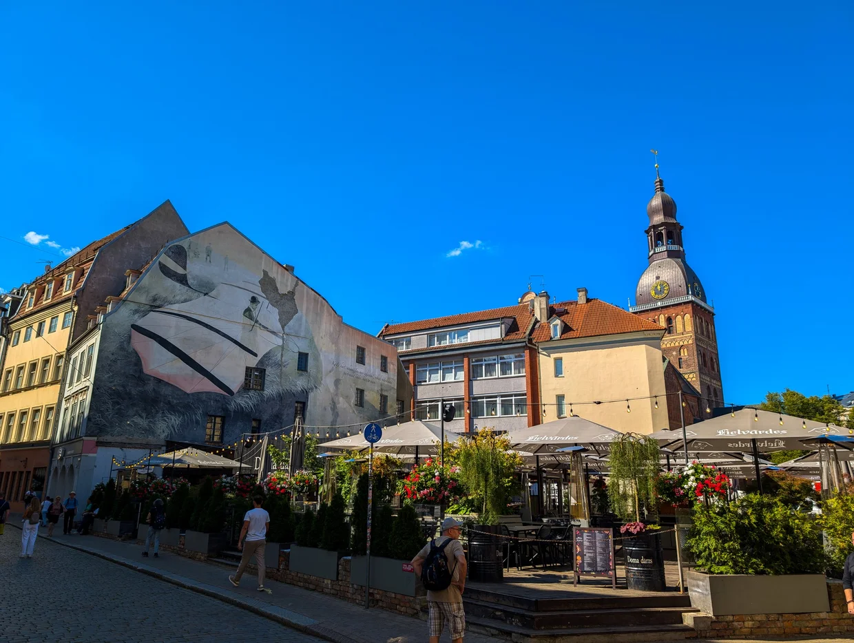 Cafes under white umbrellas in Dome Square with the Riga Cathedral visible behind