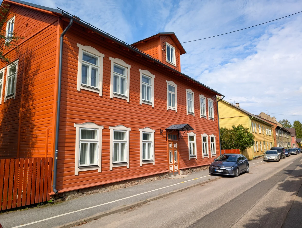 Red wooden two-story Tartu house with white window frames on a quiet street