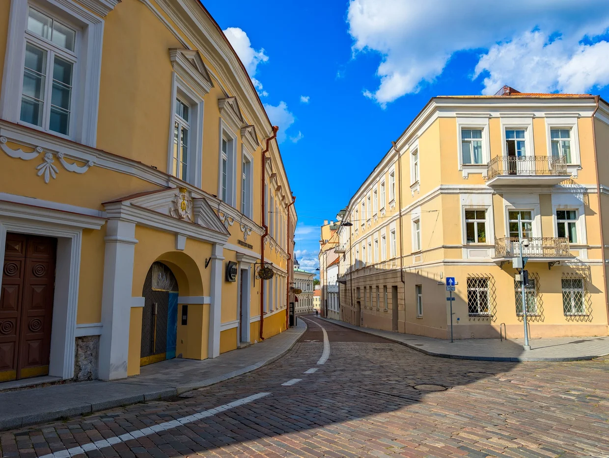 Curved cobblestone street junction in Vilnius with yellow and cream facades