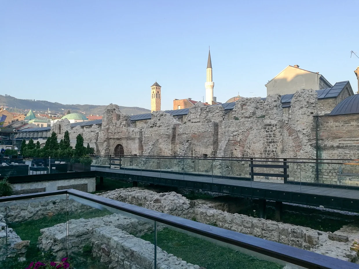 Archaeological ruins in Sarajevo with a minaret and clock tower behind