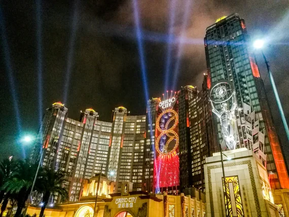 Studio City Macau casino lit up at night with spotlights and golden figure-eight ferris wheel