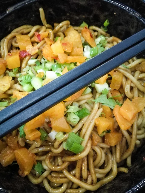 Bowl of spicy noodles with vegetables and chopsticks
