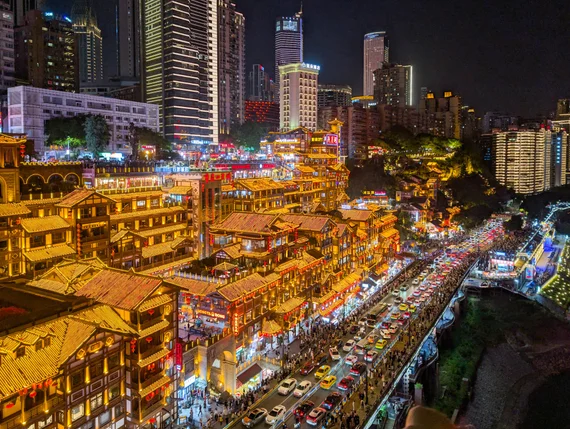 Chongqing Hongyadong stilted building complex lit up at night with skyscrapers behind