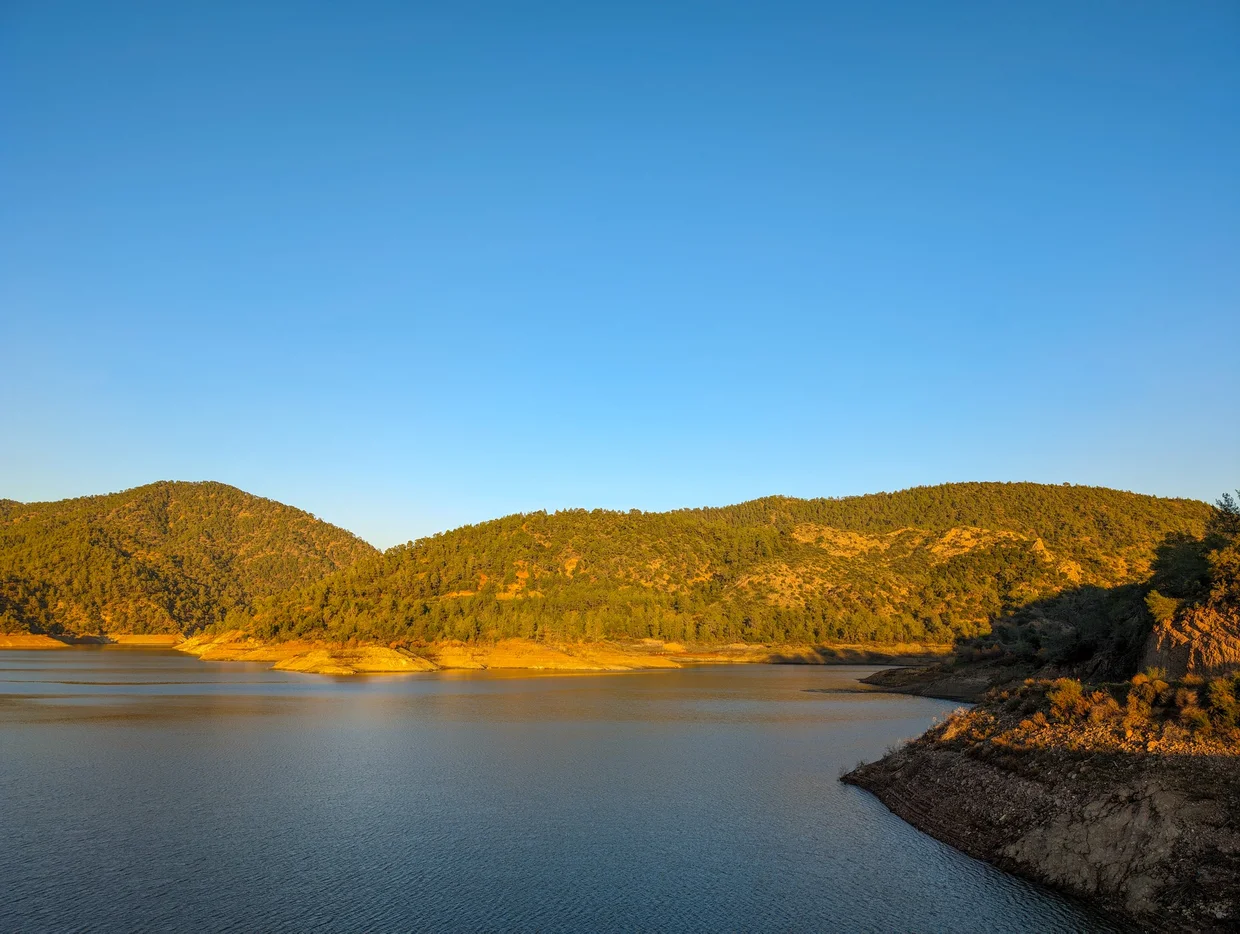 Reservoir surrounded by forested green hills in golden hour light