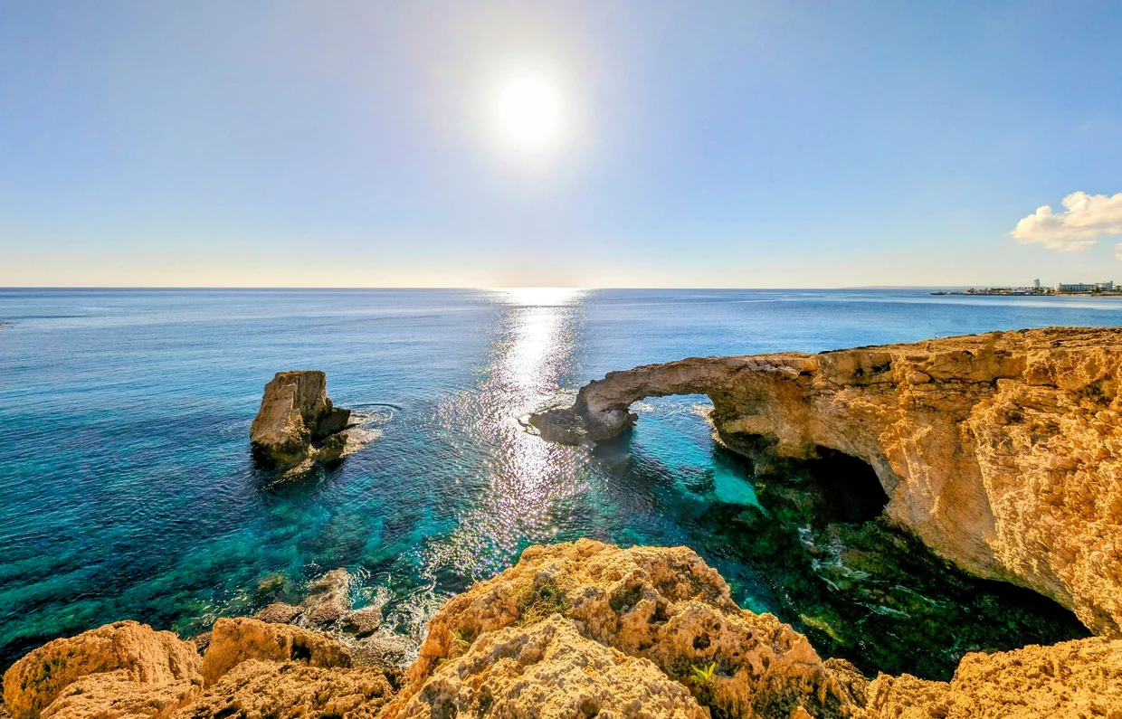 The Love Bridge natural rock arch at Cape Greco with sun reflecting on the sea