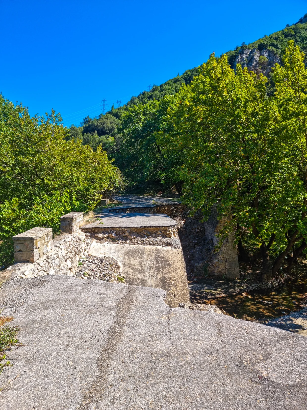 Damaged old stone bridge with a large section collapsed into a stream