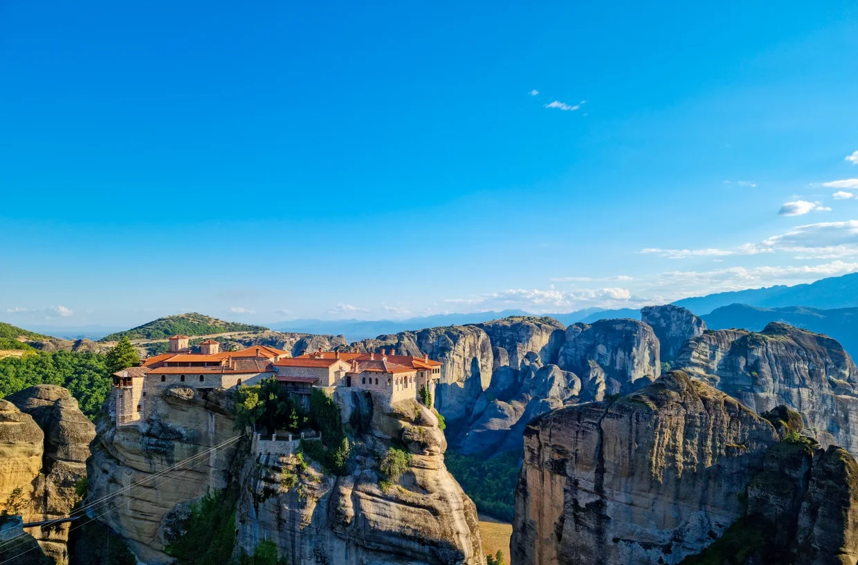 Monastery buildings clinging to a clifftop above a forested valley