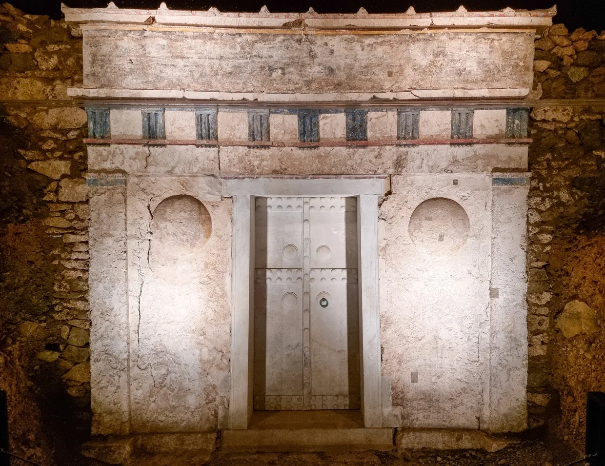 Painted facade of a Macedonian tomb at Vergina with marble double doors, illuminated underground