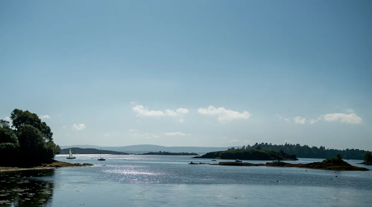 Calm bay with a sailboat and wooded islands sparkling in the sunlight