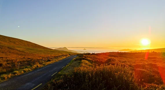 Narrow coastal road at sunset with Skellig Islands on the horizon