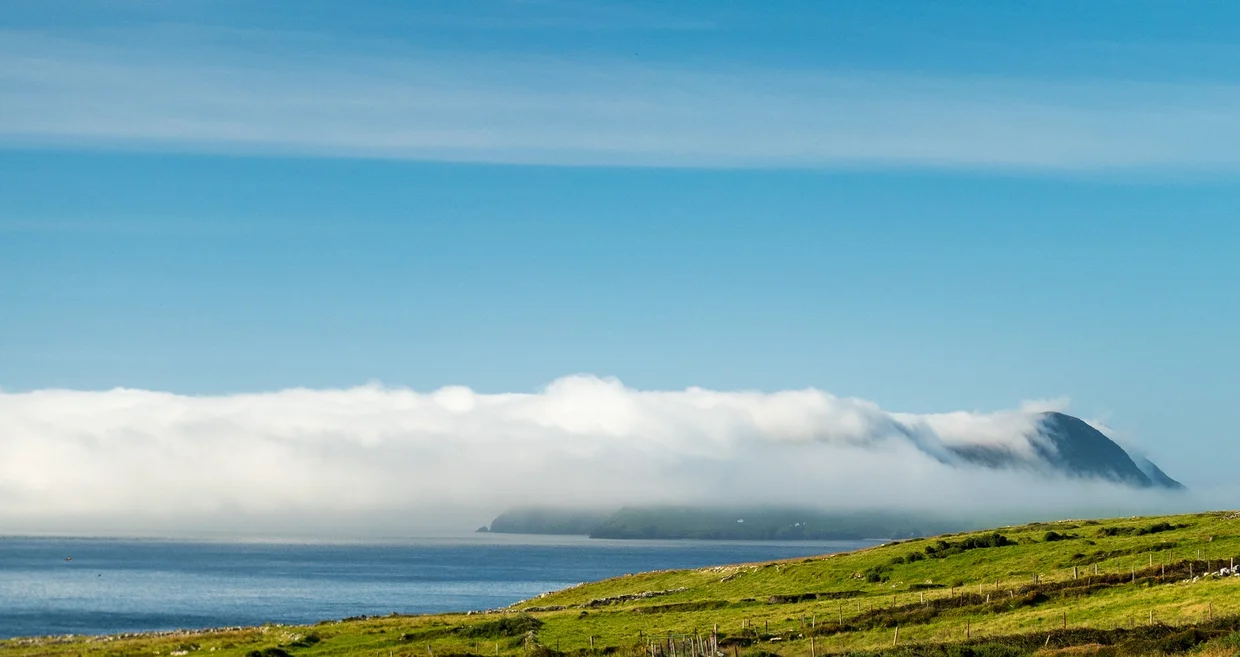 Mountain headland wrapped in low sea cloud, green fields in the foreground