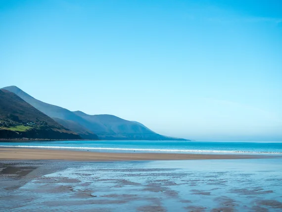 Beach at the foot of green mountains, waves lapping at the shore