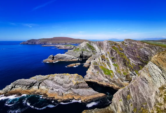 Rugged Kerry coastline with layered rock formations and green fields