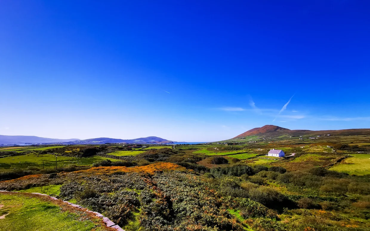 Rolling green countryside with scattered farmhouses and mountains
