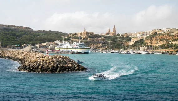 Ferry docked at Mgarr with speedboat cutting through turquoise water