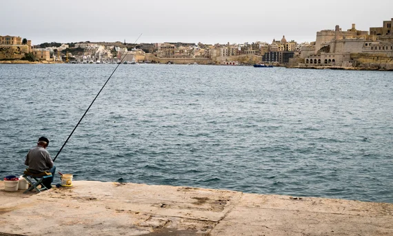 Man fishing from the quay with Valletta's skyline behind