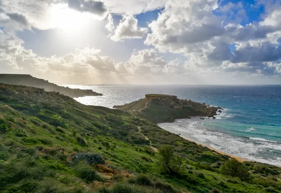 Green coastal hillside leading to a rocky bay with turquoise water