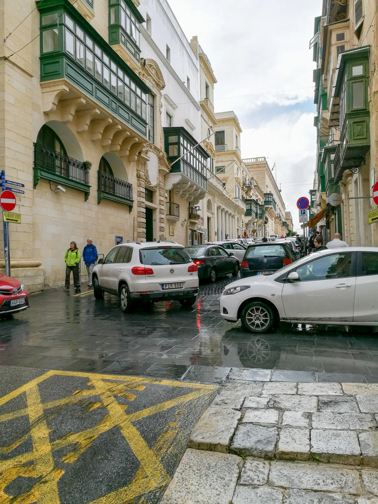 Rainy day in a Maltese town with limestone buildings and green balconies