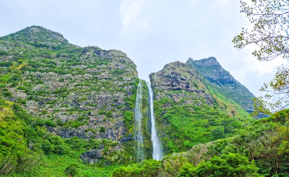 Tall waterfall plunging down a rocky green cliff face near Fajã Grande
