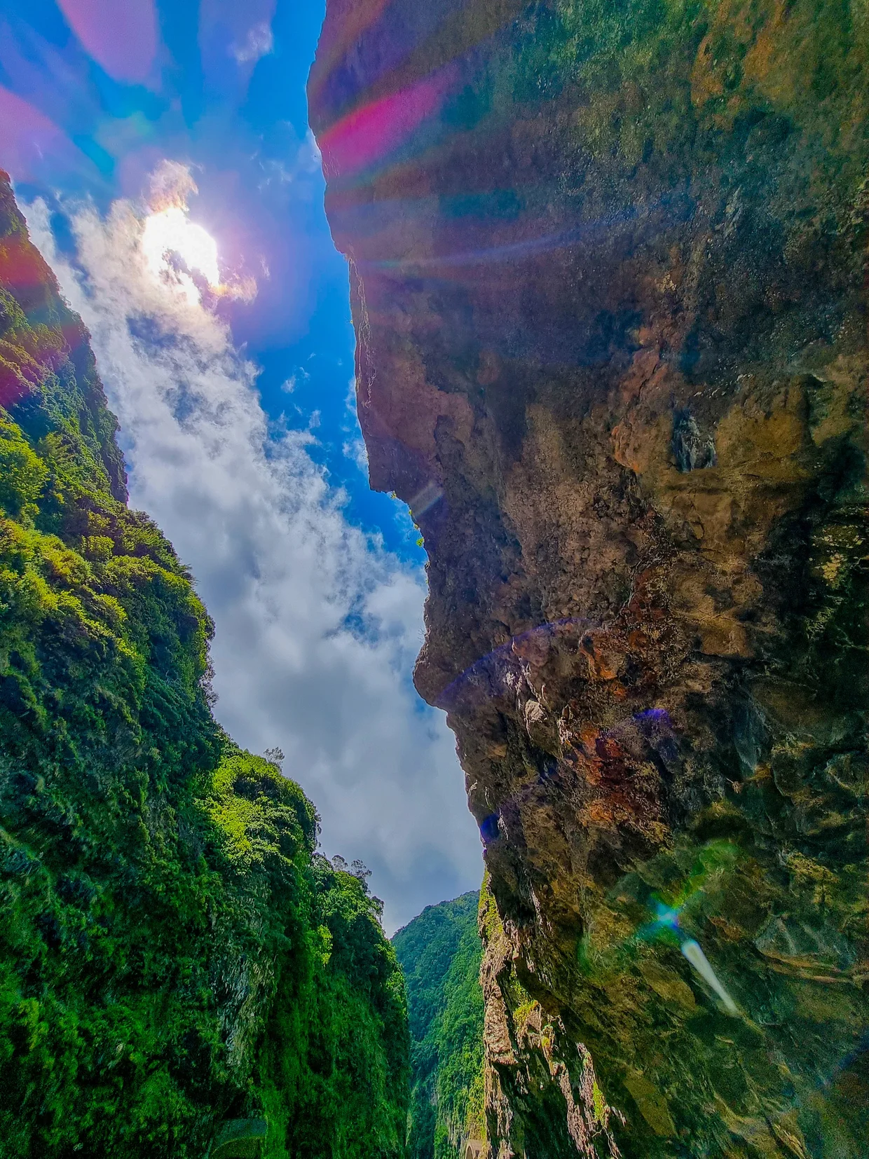 Looking straight up from inside a deep gorge, sun rays breaking through between massive cliff walls