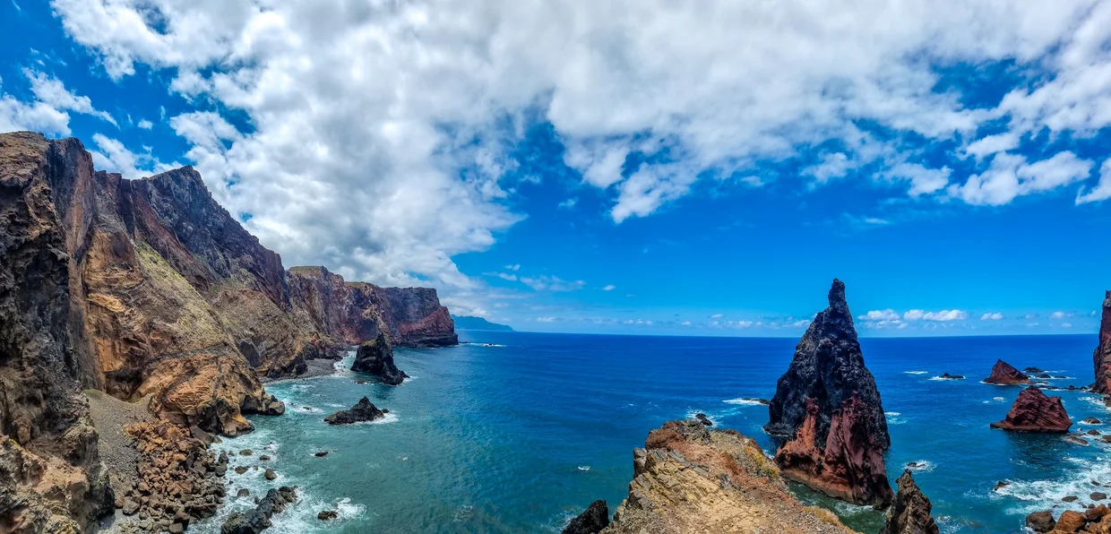 Wide panoramic view of Ponta de São Lourenço, volcanic cliffs and sea stack against blue sky