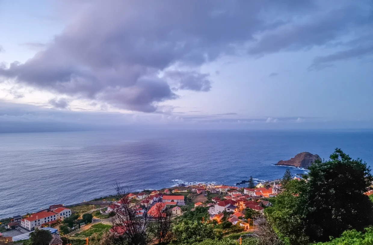 Porto Moniz town at dusk, orange rooftops against purple sky, volcanic islet offshore