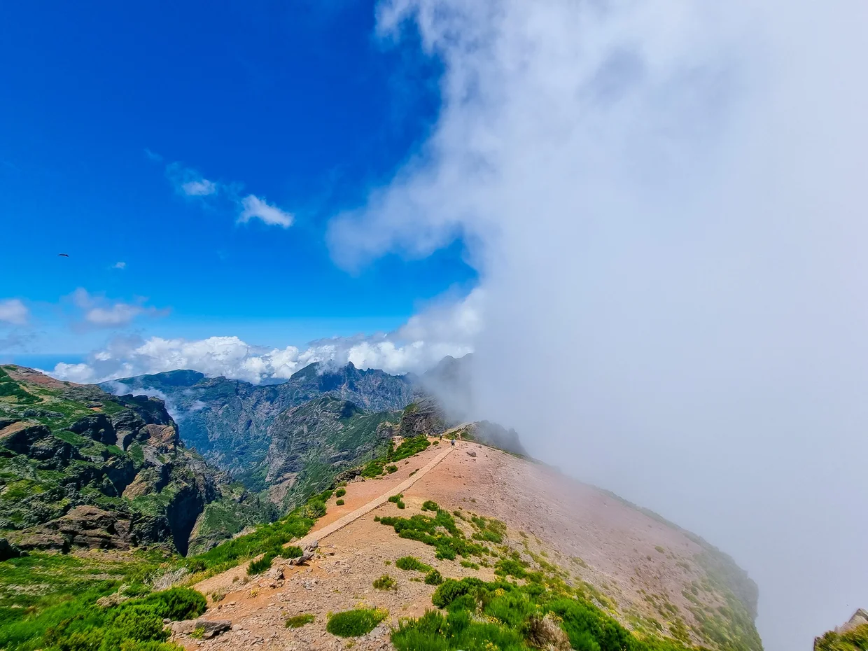 Ridge trail disappearing into a wall of clouds, mountain slopes falling away on both sides