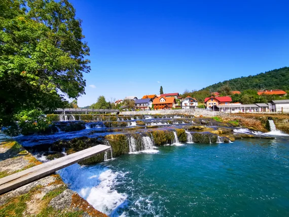 Bright turquoise cascades on the Krka river with a village behind