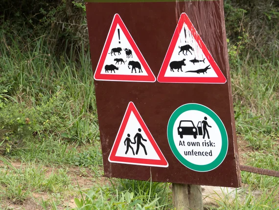 Warning sign for unfenced wildlife area with pictograms of hippos, crocodiles, and other dangers