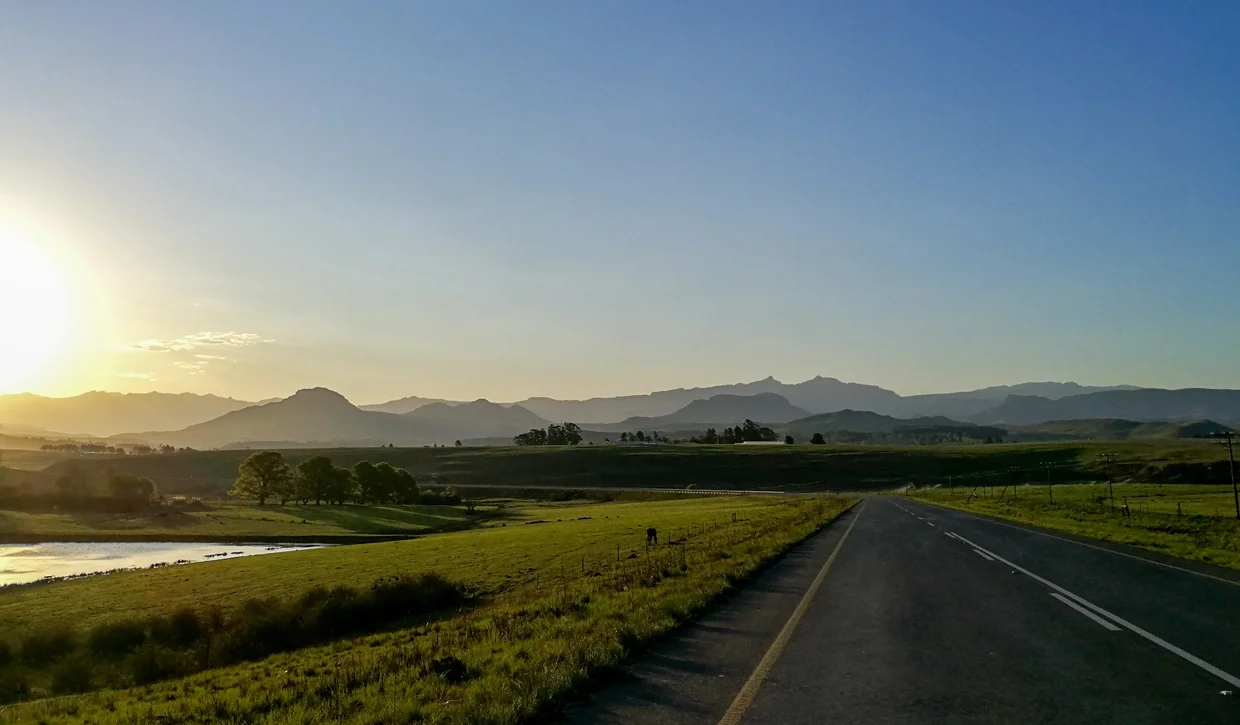 Road near Underberg at sunset with green farmland and the Drakensberg silhouette
