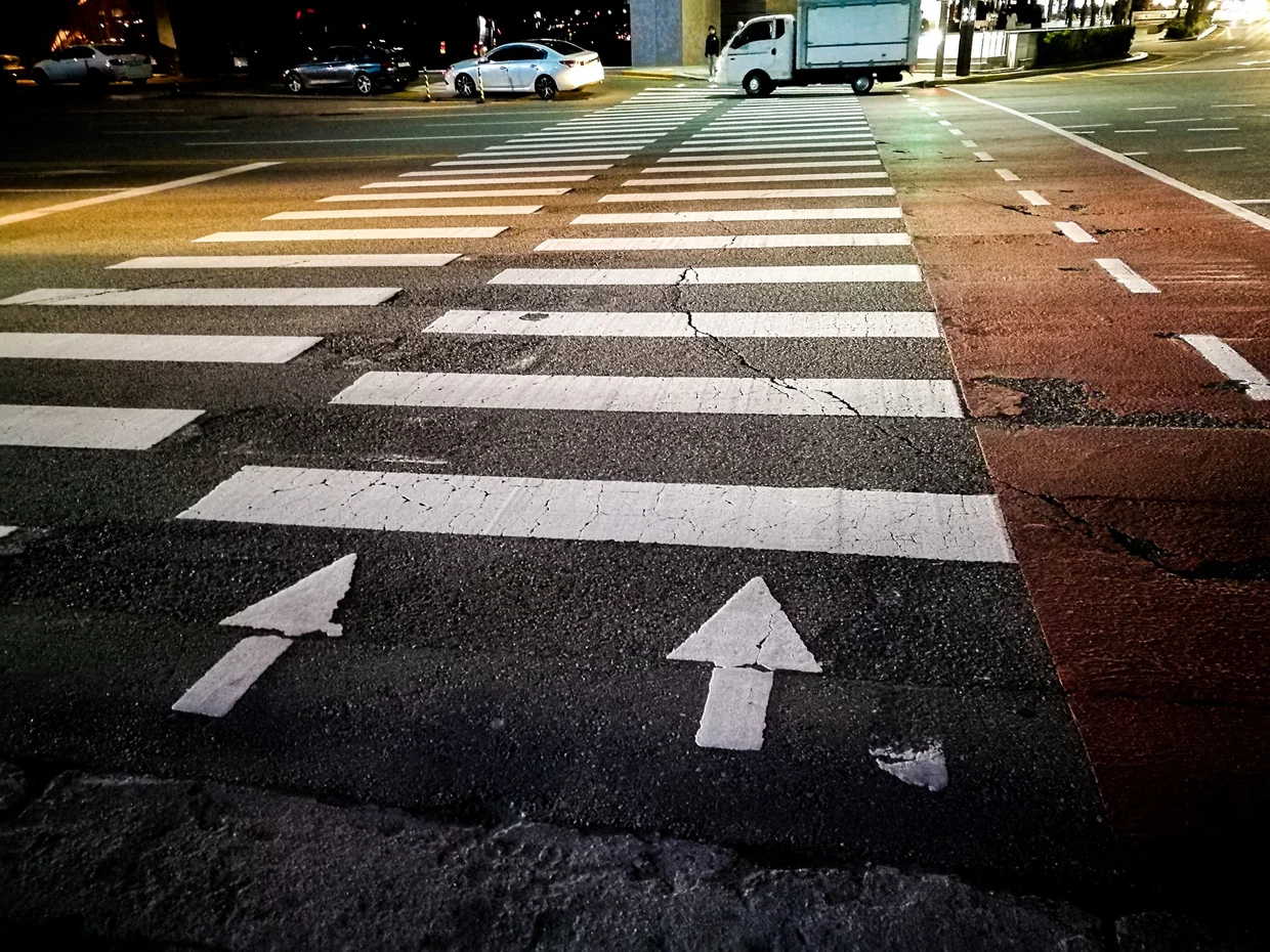 Night crosswalk with white arrows, empty and moody under streetlights