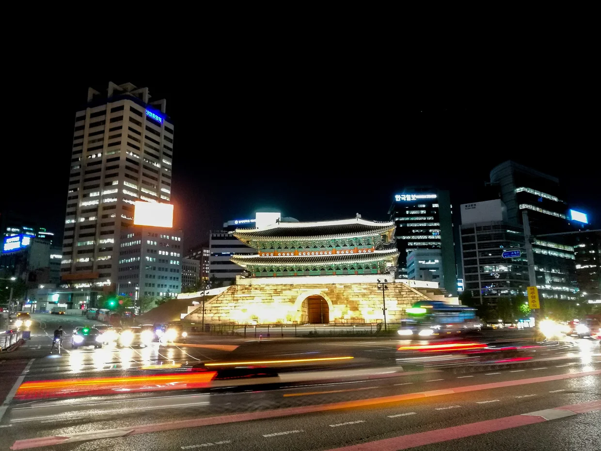 Namdaemun Gate at night, illuminated gold against modern office buildings and traffic light trails