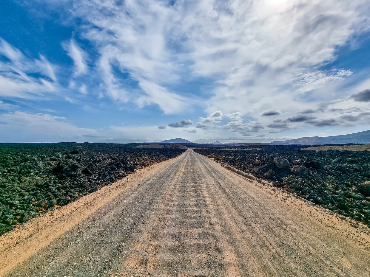 Straight dirt road cutting through lava fields toward distant mountains