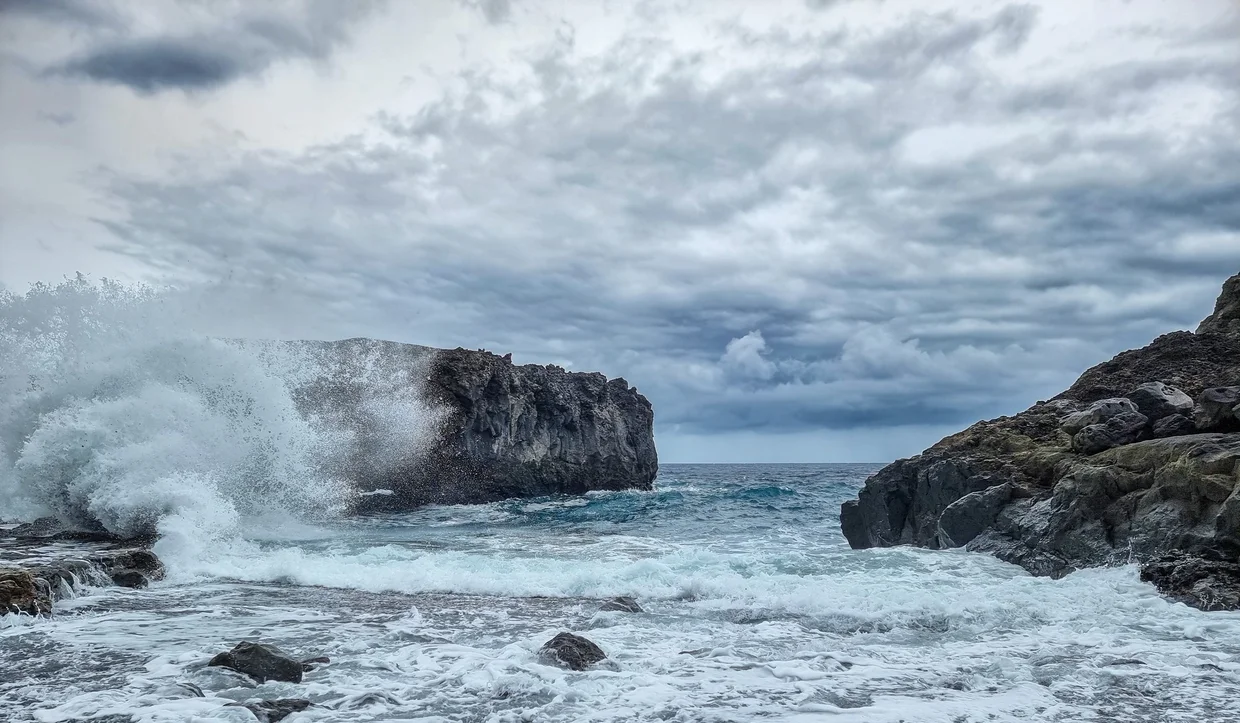 Waves crashing explosively against dark volcanic rock cliffs