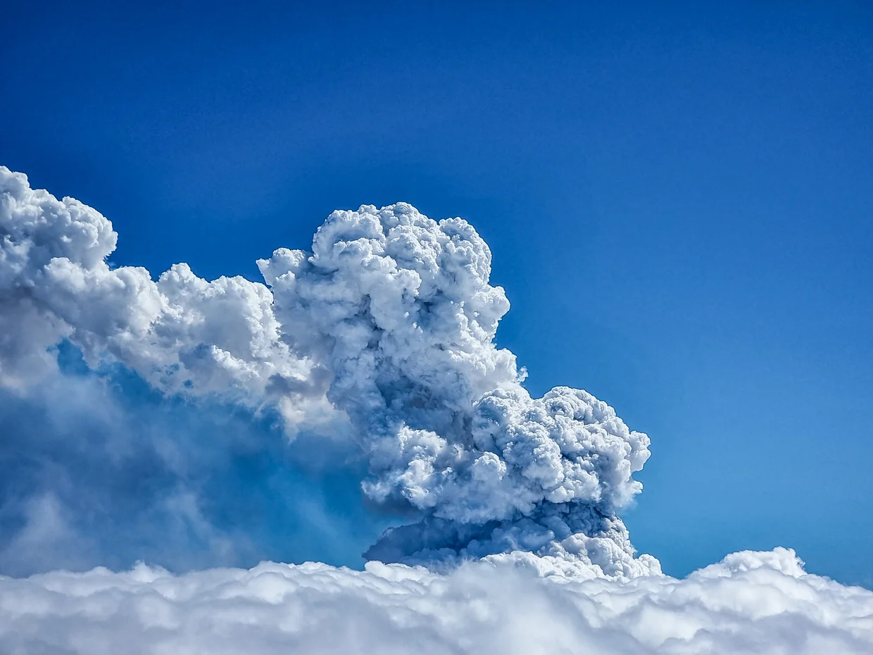 Massive volcanic ash and steam plume rising above the cloud layer into blue sky