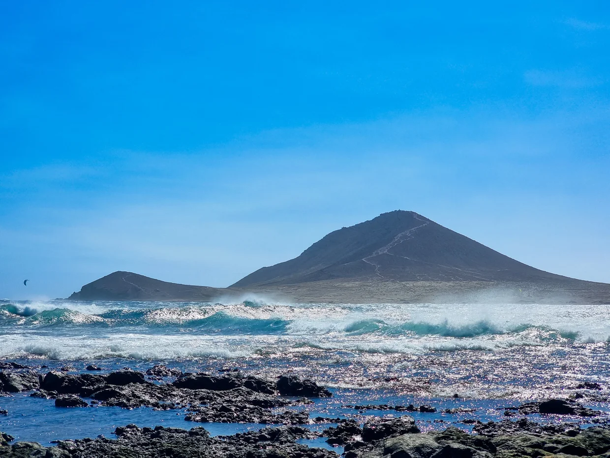 Volcanic mountain rising from ocean with rough waves and mist