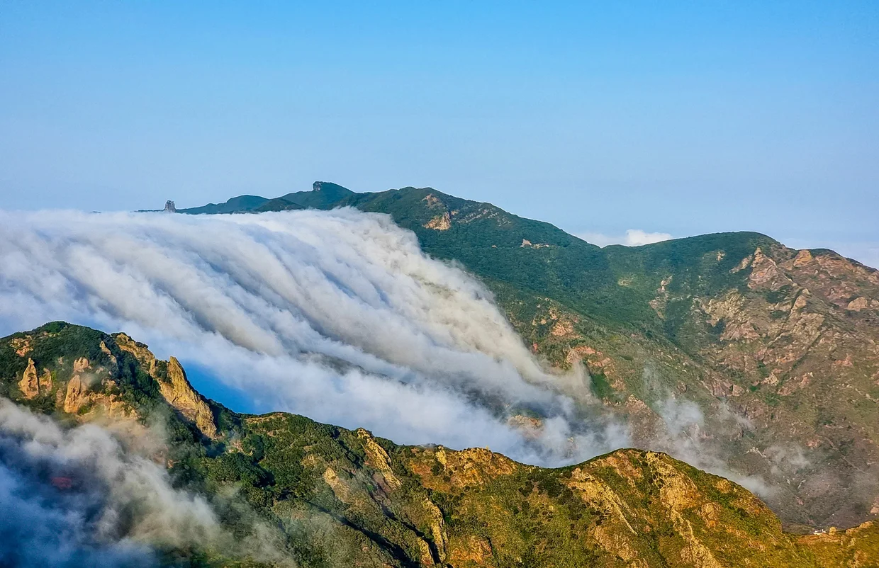 Clouds cascading like a waterfall over a green mountain ridge