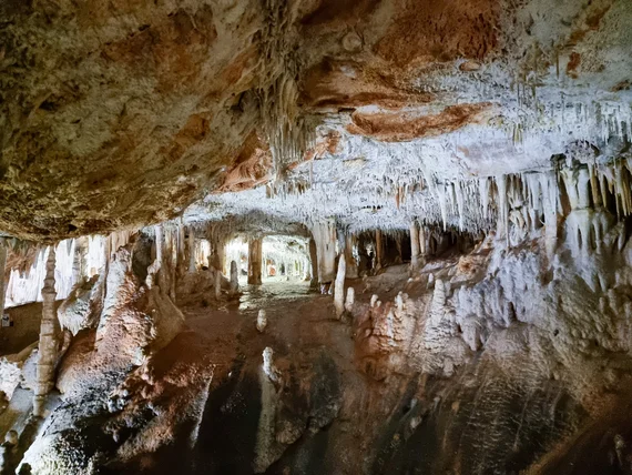 Cave interior with stalactites, stalagmites, and reflections in underground pool