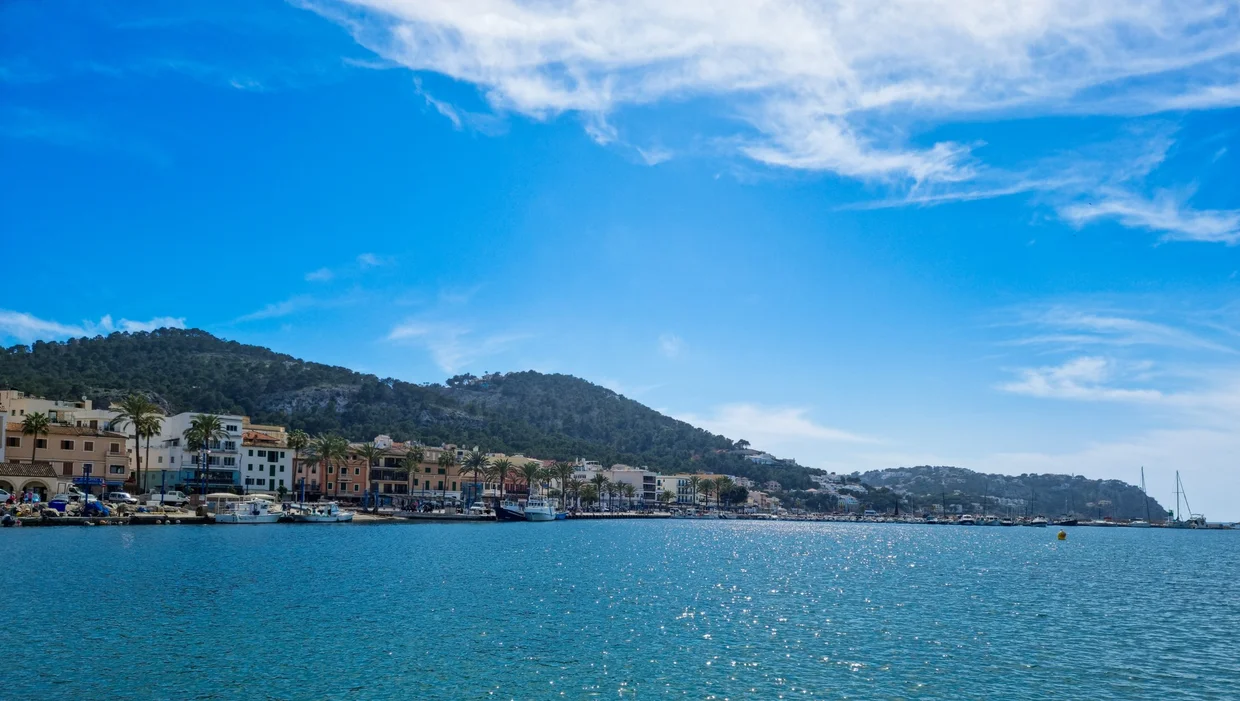 Harbor town with colorful facades, green hillside, and sparkling blue sea