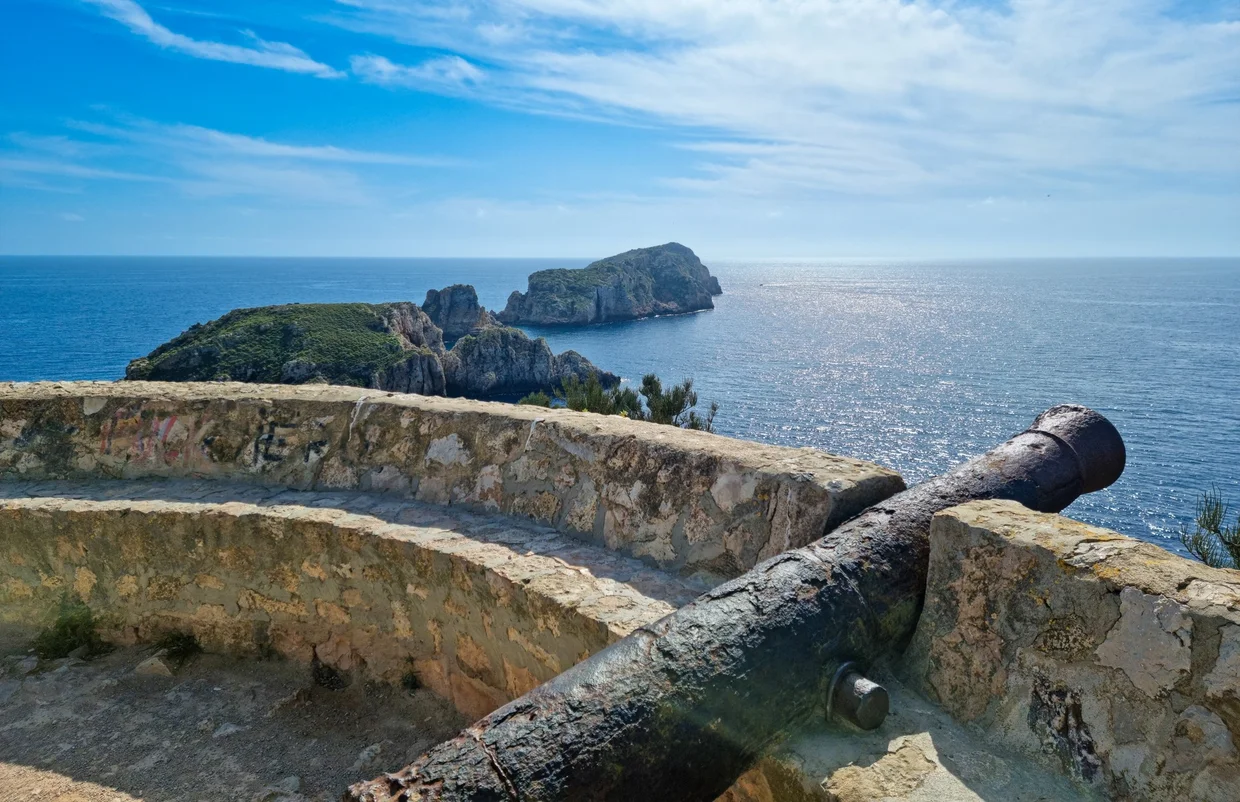 Historic cannon on fortress wall, rocky headland and glittering sea beyond