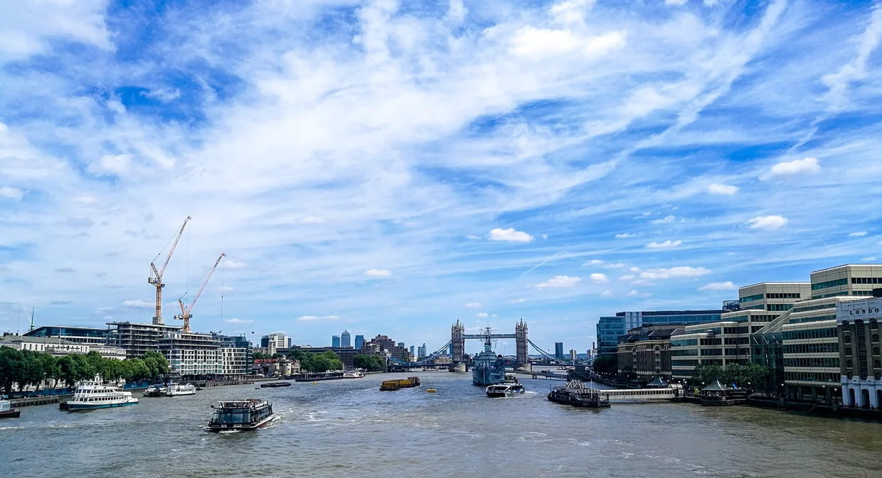 The Thames stretching toward Tower Bridge, boats on the water, blue sky and clouds above