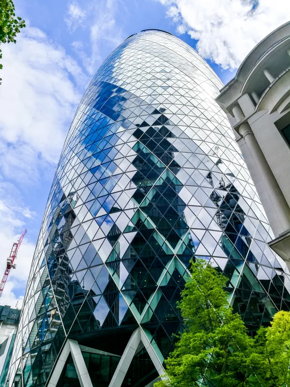 The Gherkin's diamond glass panels up close, a green tree at its base
