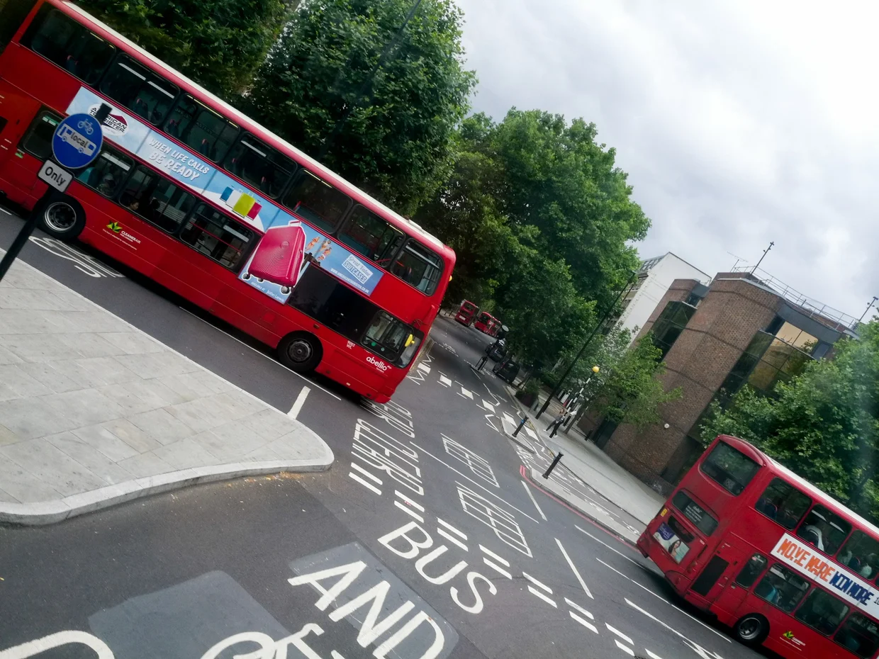 Two red double-decker buses at a bus stop, bus lane markings on the road