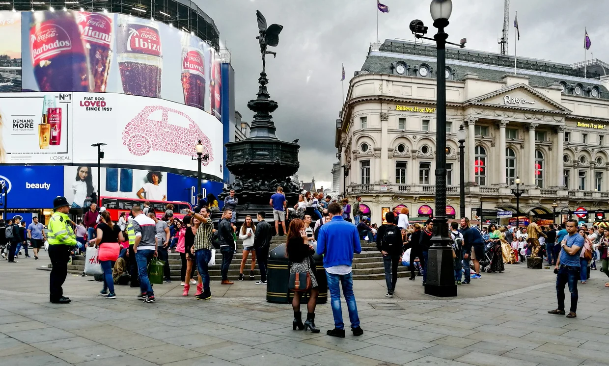 Piccadilly Circus with the Eros statue, neon billboards, and crowds on an overcast day