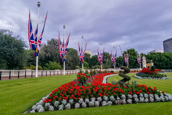 Union Jack flags lining the path near Buckingham Palace, red flower gardens in bloom
