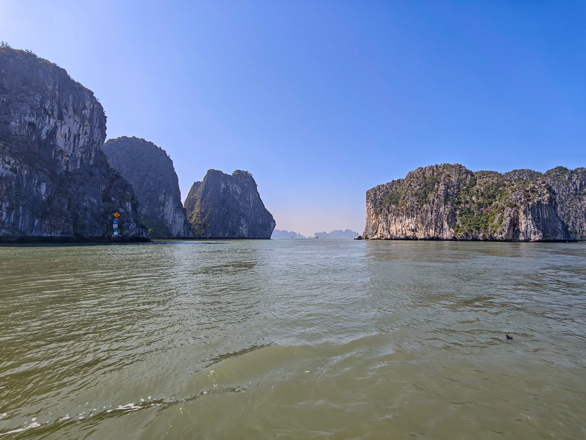 Ha Long Bay seascape with scattered green islands and a cloudy sky, viewed from a moving tour boat