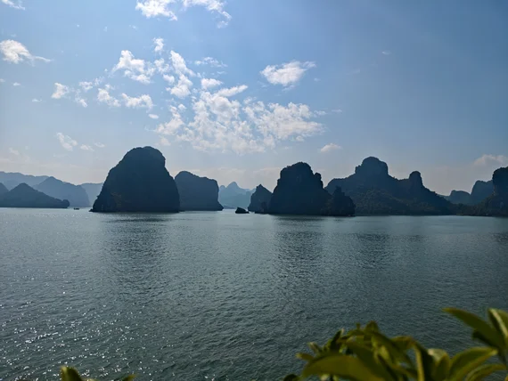 Ha Long Bay limestone pillars covered in greenery emerging from misty water, photographed from a boat