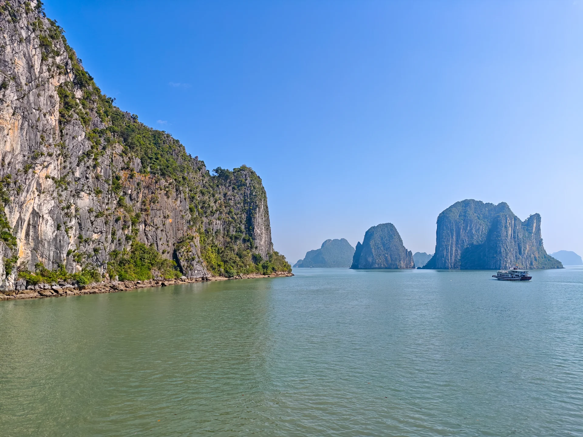 Close-up of steep limestone karst cliffs rising vertically from the calm sea in Ha Long Bay, Vietnam
