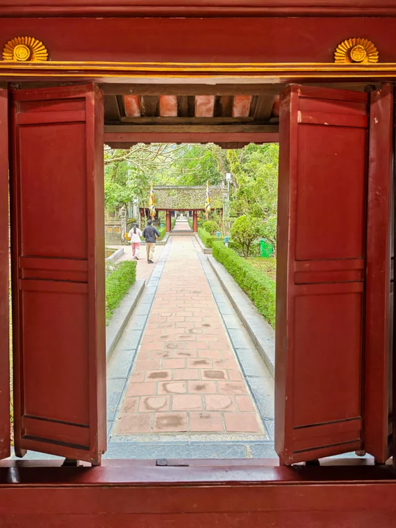 View through red wooden temple shutters toward a paved Hoa Lu walkway
